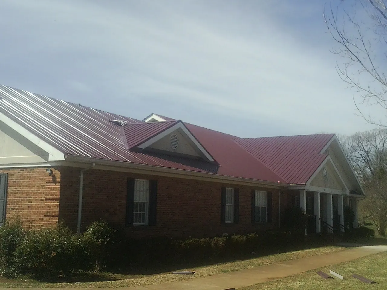 Red metal roof with gabled entries on a long brick building, from a Hail Damage Roof Repair job in Picayune