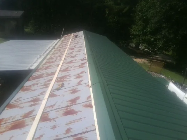 Old rusted panels beside newly installed green metal roofing — Wind Damage Roof Repair by Roofing Brothers in Picayune