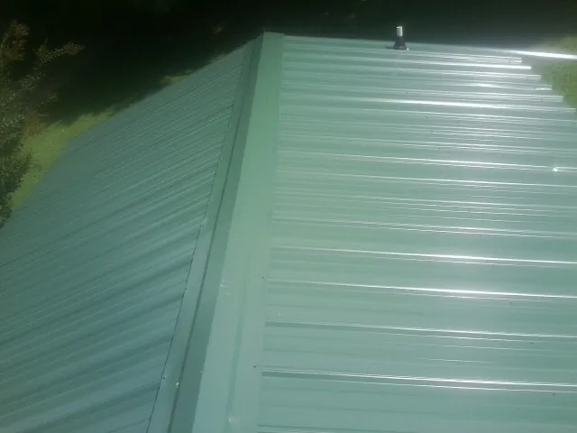 New green metal panels meeting at the ridge of a roof — Flat Roof Repair work by our crew in Picayune