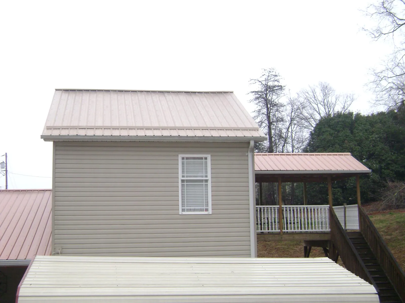 Tan metal roofs on a two story addition and attached porch, from a Roof Replacement job in Picayune